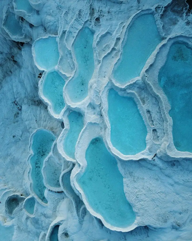 A stunning aerial view of natural turquoise hot springs pools among unique white limestone formations, showcasing nature's beauty.