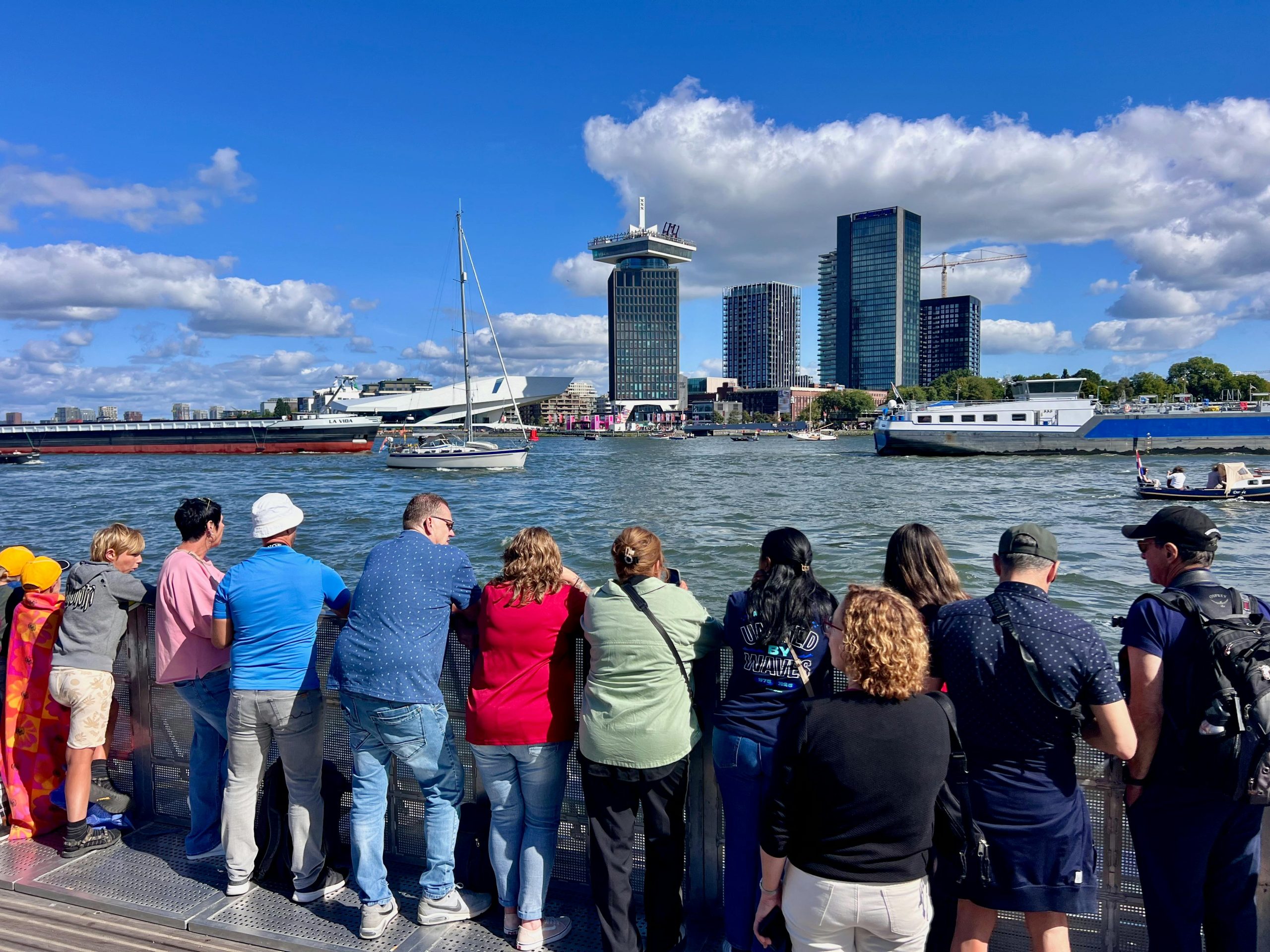 People gather to enjoy a vibrant view of Amsterdam's waterfront with iconic skyline.